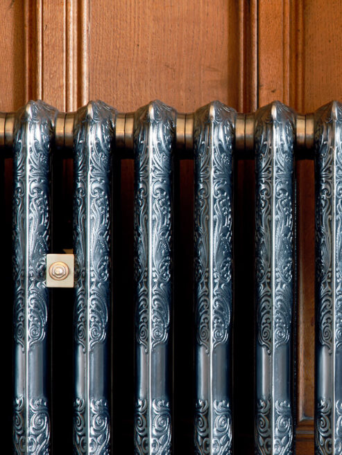 Detail ornate Rococo II cast iron radiator in Full Polish in wood paneled room