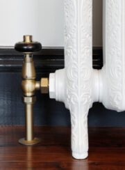 RadCen Traditional TRV Valve Set Finished in a Natural Brass with matching pipe covers on a white radiator and dark hard wood floor