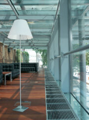 Fan assisted hybrid trench heating/cooling system for heat pumps with natural aluminium grille on wooden floor and standard lamp