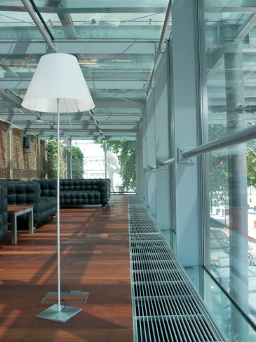 Fan assisted hybrid trench heating/cooling system for heat pumps with natural aluminium grille on wooden floor and standard lamp