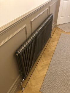 Bare Metal Lacquer Traditional Tuba Classic Steel Column radiator in North London Hallway on parquet flooring and wood paneling and rug