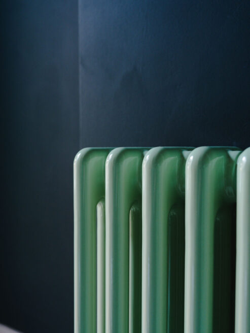 Mint green steel Tuba radiator shown against dark wall