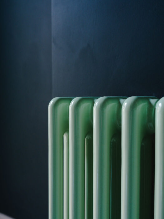 Mint green steel Tuba radiator shown against dark wall