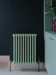 Steel Tuba traditional radiator shown in mint green RAL6019 against dark green wall