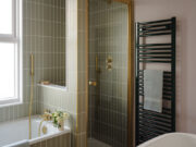 Essential towel rail in RAL6005 dark green shown in bathroom against pale green tiles and pink wall