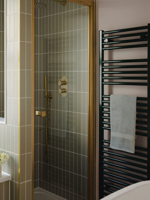Essential towel rail in RAL6005 dark green shown in bathroom against pale green tiles and pink wall