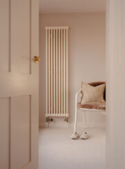 Milky White Tuba vertical radiator shown in bedroom with putty colour walls