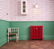 Rococo Cast Iron Radiator II in Heritage Red against green panelling.