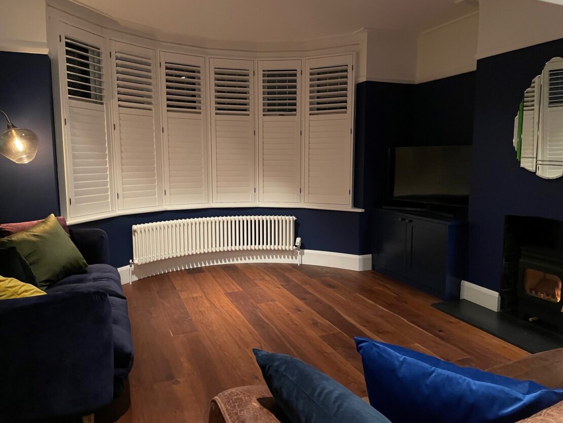 Bay windows with shutters and curved Tuba Steel Column Traditional radiator finished in white on wooden flooring