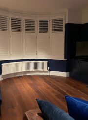 Bay windows with shutters and curved Tuba Steel Column Traditional radiator finished in white on wooden flooring