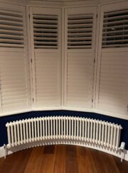 Long Bay Window Steel Column Tuba Radiator with white shutters and dark wooden floor