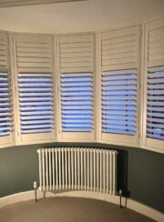 Curved Bay window Tuba Steel Column Radiator below shuttered white windows and grey wall