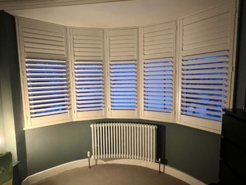 Curved Bay window Tuba Steel Column Radiator below shuttered white windows and grey wall