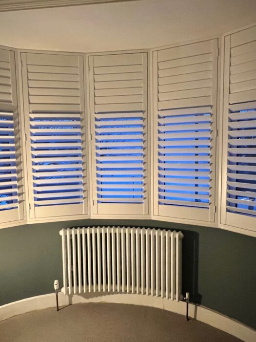 Curved Bay window Tuba Steel Column Radiator below shuttered white windows and grey wall