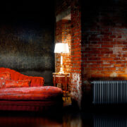 Vasco Vintage Traditional Style Steel Radiator finished in Black on exposed brick wall with table lamp and red sofa