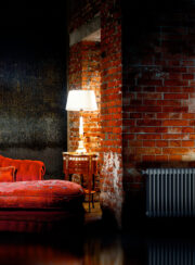 Vasco Vintage traditional Style Steel Radiator finished in Black on exposed brick wall with table lamp and red sofa
