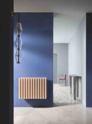 Low Soho Aluminium Contemporary Radiator in Wrinkled Ivory finish on blue wall by chandelier
