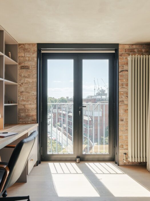 White vertical column radiator on exposed brick wall with floor to ceiling curtains